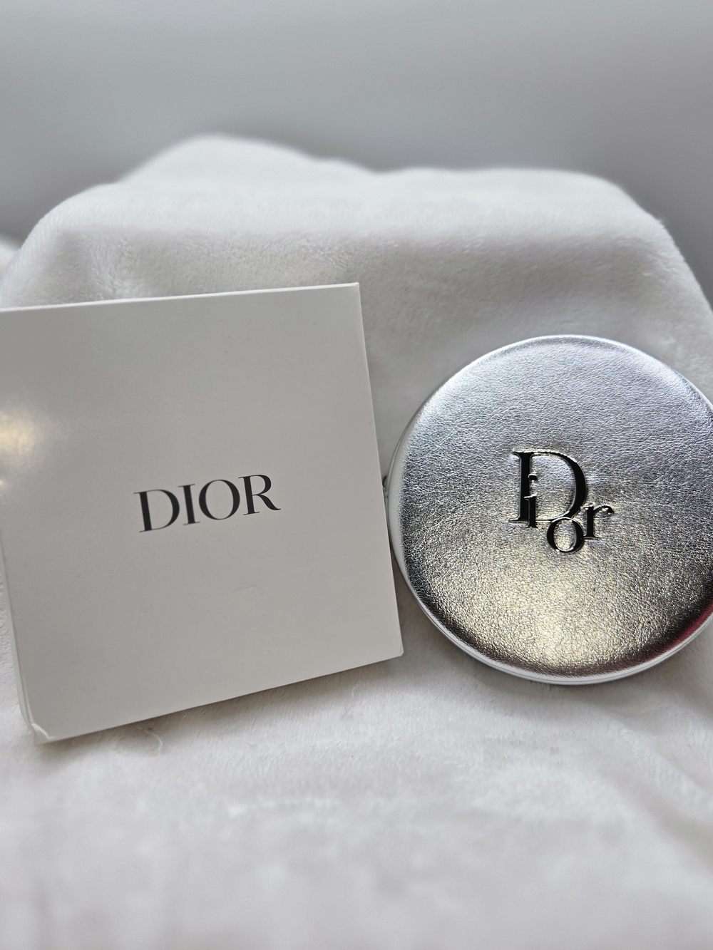 Round cosmetic pouch in metallic silver finish featuring raised logo